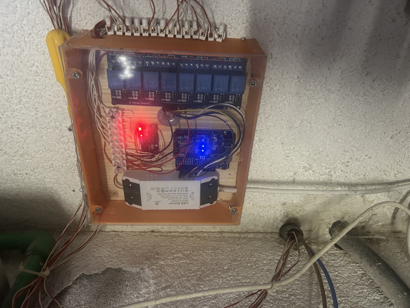 The wall box after five years: an eight-channel relay board, a Wemos D1 mini with its status LED lit, screw terminal blocks for the garden wiring, and a 12 V LED driver
